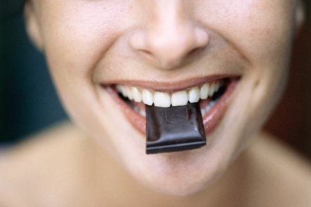 Pessoa com um pedaço de chocolate preto na boca - Metrópoles