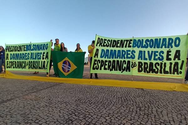Fotografia colorida de pessoas segurando duas faixas e uma bandeira do Brasil