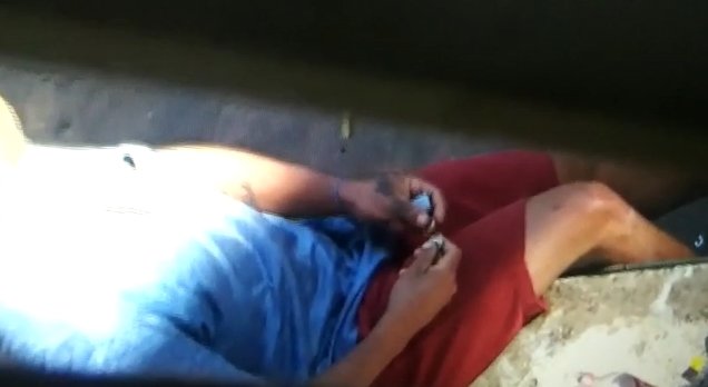 Pessoa de camisa azul e short vermelho segura pedra de crack