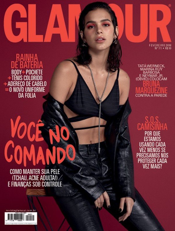 A atriz Bruna Marquezine, uma mulher branca, jovem e com cabelo castanho curto, posando para foto na capa da revista Glamour Brasil. Ela usa um top preto com amarrações e um conjunto de calça e jaqueta, ambos pretos e de couro.
