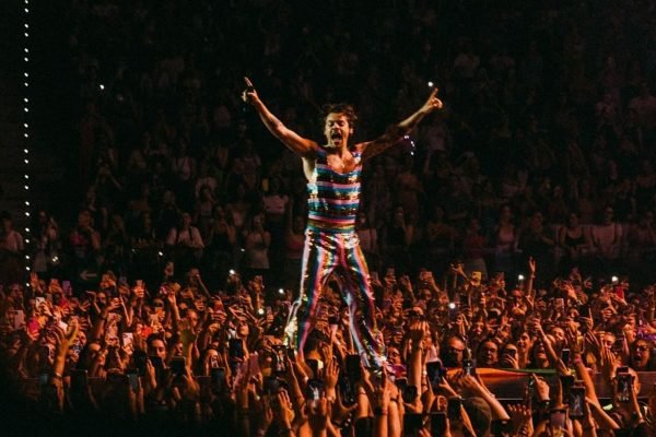 Com multidão em volta, Harry Styles em cima de palco, durante show da Love on Tour, usando look listrado e colorido da Gucci