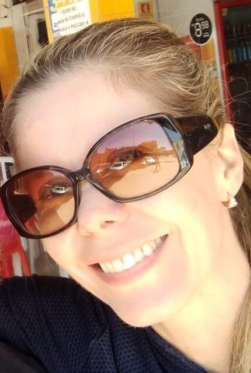 Mulher branca e loira sorrindo com o rosto de lado e usando óculos