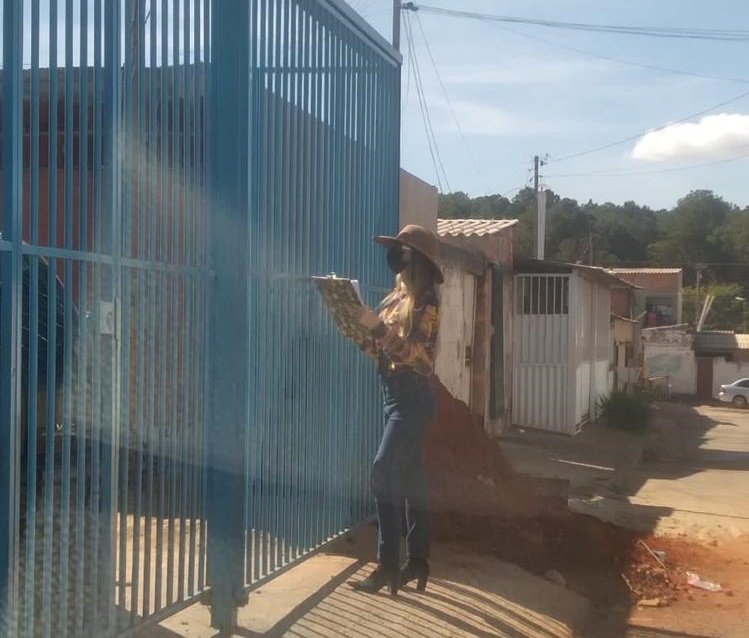 Mulher com chapeu em frente a portão de casa
