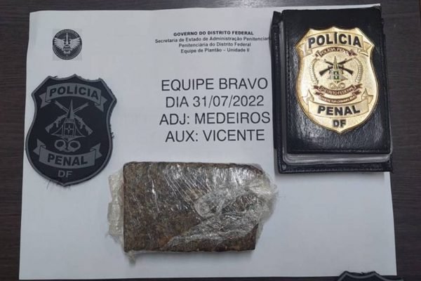 tablete escuro junto a um distintivo dourado da Polícia Penal