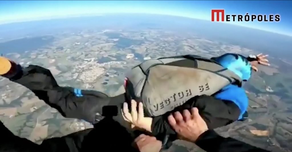 O instrutor segura a manga do macacão do aluno que mostra que sabe a localização da manopla para abrir o paraquedas