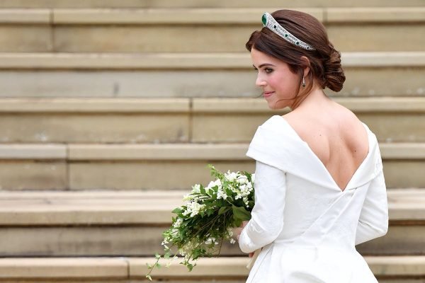 Princesa Eugenie com vestido de noiva. Na imagem, ela está de costas em uma escada, segurando um buquê