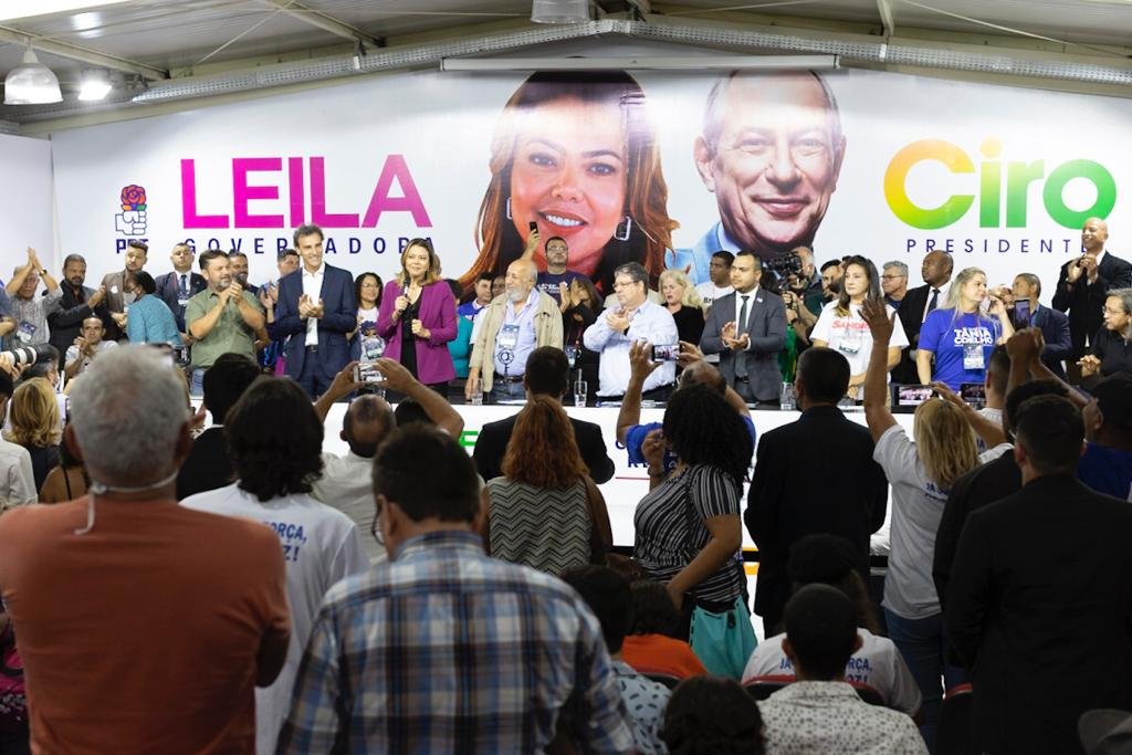 Pessoas de costas olhando para palco cheio de gente