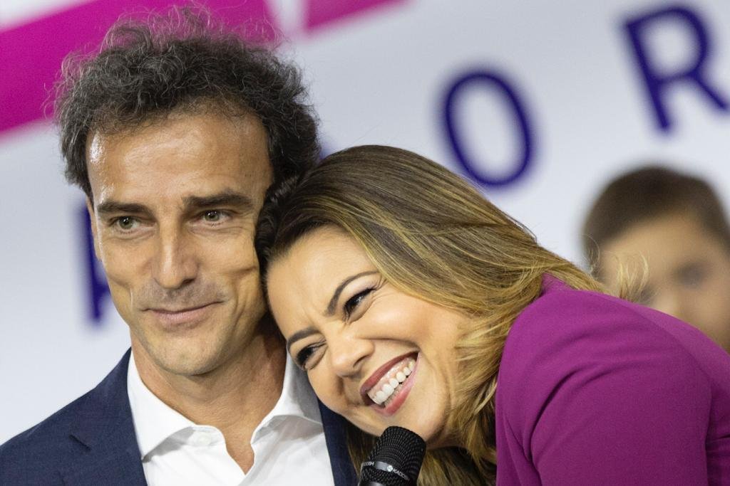 Mulher com blazer roxo com a cabeça deitada em ombro de homem e sorrindo