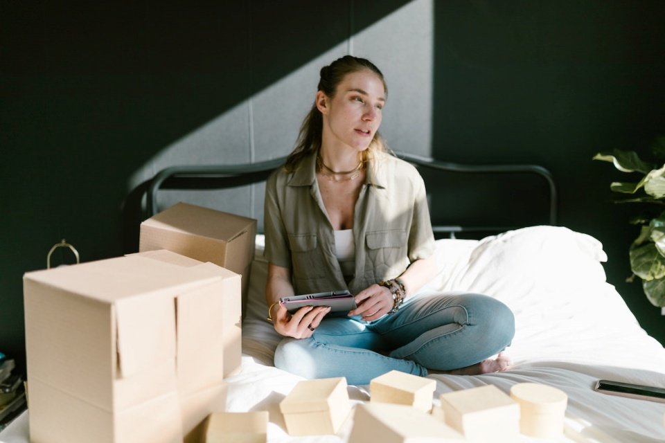 Jovem mulher sentada na cama com caixas ao lado
