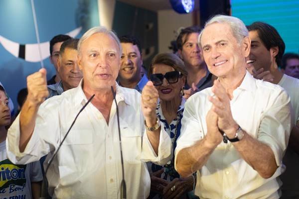 Fotografia colorida de dois homens discursando em micronfones