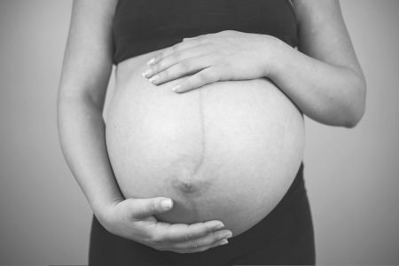 Imagem em preto e branco de mulher grávida com as mãos na barriga - Metrópoles