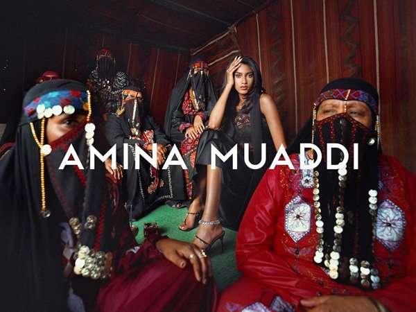 Campanha de divulgação da marca de sapatos Amina Muaddi. Na foto, é possível ver uma mulher no centro, com a sandália de salto da marca, e outras mulheres vestidas de modo típico árabe