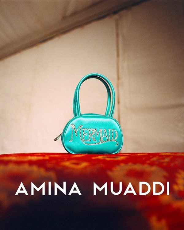 Campanha de divulgação da marca de sapatos Amina Muaddi. Na foto, é possível ver uma bolsa azul turquesa com brilhos rosa que formam a palavra Mermaid, sereia em inglês