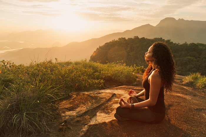 Mulher sentada em uma montanha fazendo meditação - Metrópoles