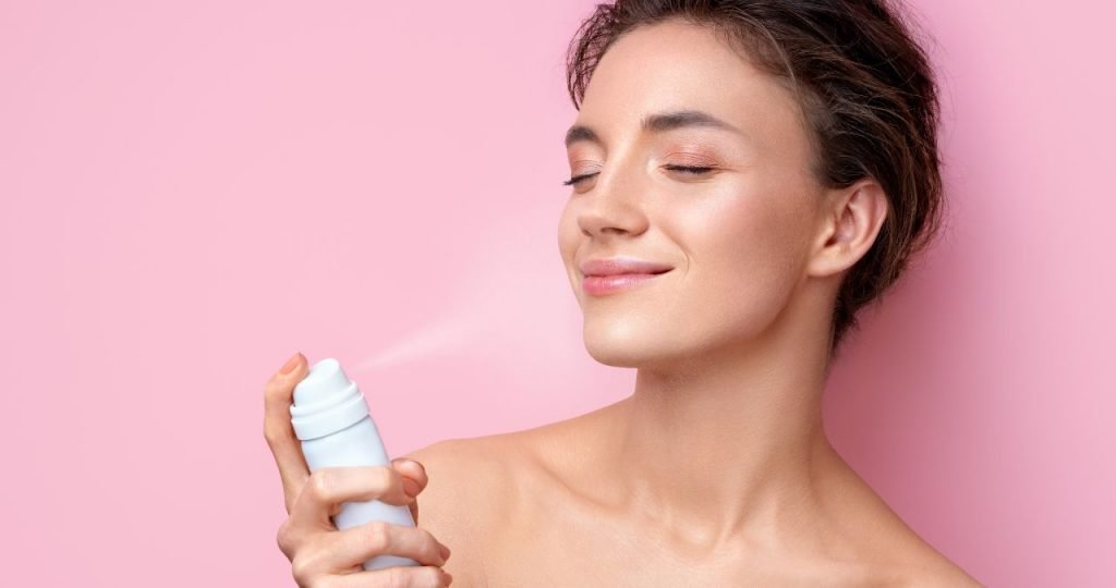 Mulher passando água termal no rosto em um fundo rosa - Metrópoles