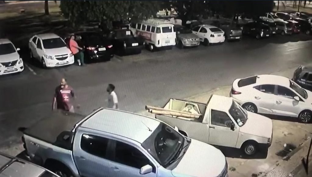 Homem de camisa roxa anda pelo estacionamento