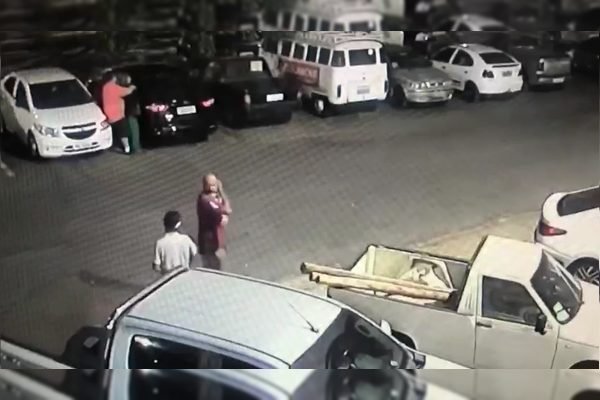 Homem de camisa roxa anda pelo estacionamento