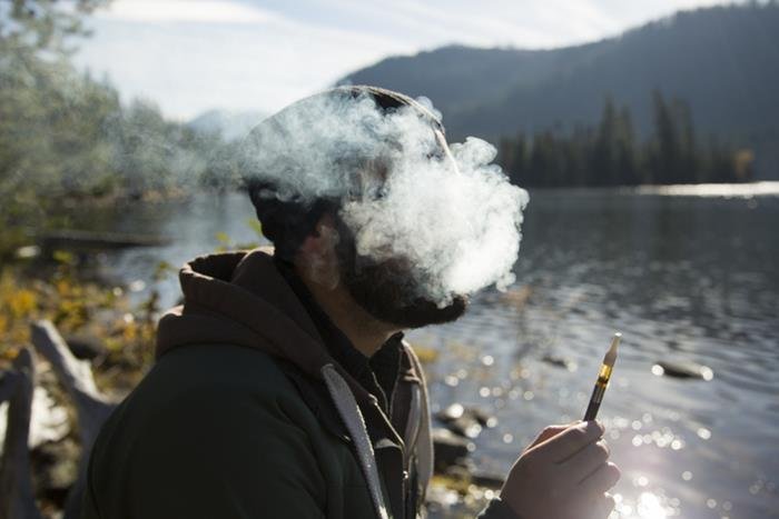 Homem sentado em frente a um lago fumando - Metrópoles