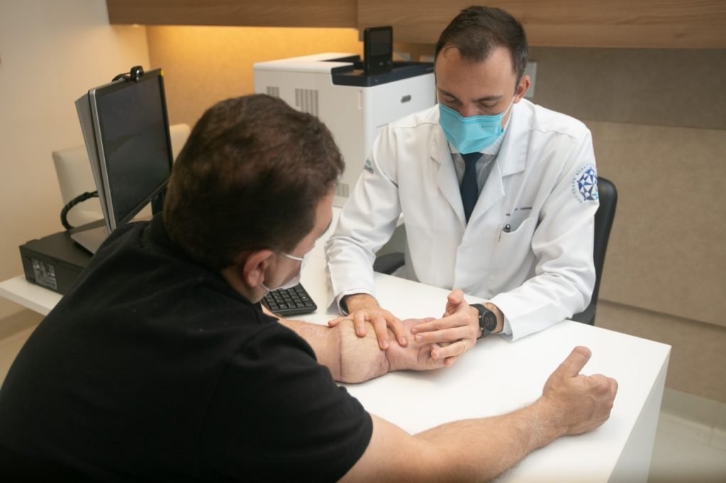 fotografia colorida de médico avaliando braço reimplantado do paciente em um consultório