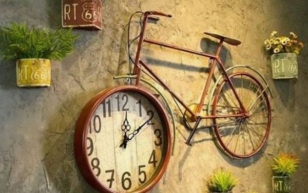 Imagem colorida de uma bicicleta grudada na parede em que uma de suas rodas é adaptada para ser um relógio