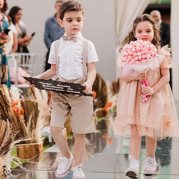 Duas crianças, um menino e uma menina, ambos brancos e com cabelos castanhos, andando pelo altar em um casamento.