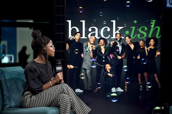 A atriz Marsai Martin, uma mulher jovem e negra, de cabelos trançados, em um programa de TV falando sobre a série Black-ish
