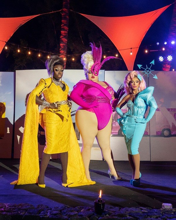Três drag queens participantes da série We're Here, da HBO. Na foto, as três aparecem com roupas extravagantes e com outras pessoas não montadas de drags