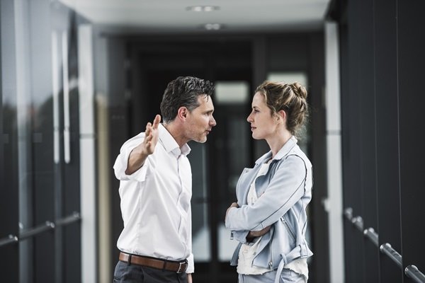 Homem e mulher, ambos brancos e adultos jovens, discutindo em uma sala no ambiente de trabalho
