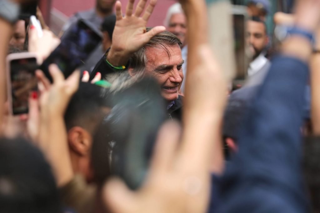 Candidato à reeleição, Jair Bolsonaro (PL) cumprimenta apoiadores na saído do Bar da Dirce, em São Paulo. Ele acena para as pessoas no meio de uma multidão, usando jaqueta preta - Metrópoles