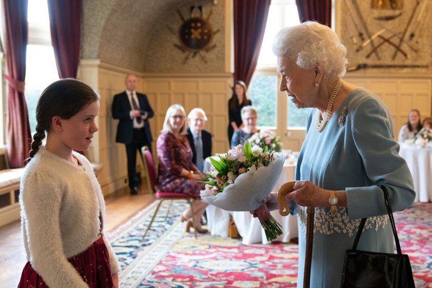 Foto colorida. Menina entrega flores para senhora idosa