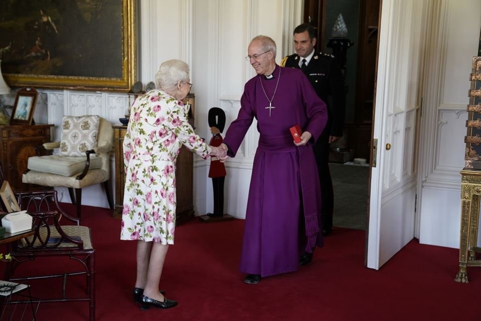 Foto colorida. Mulher idosa cumprimenta padre