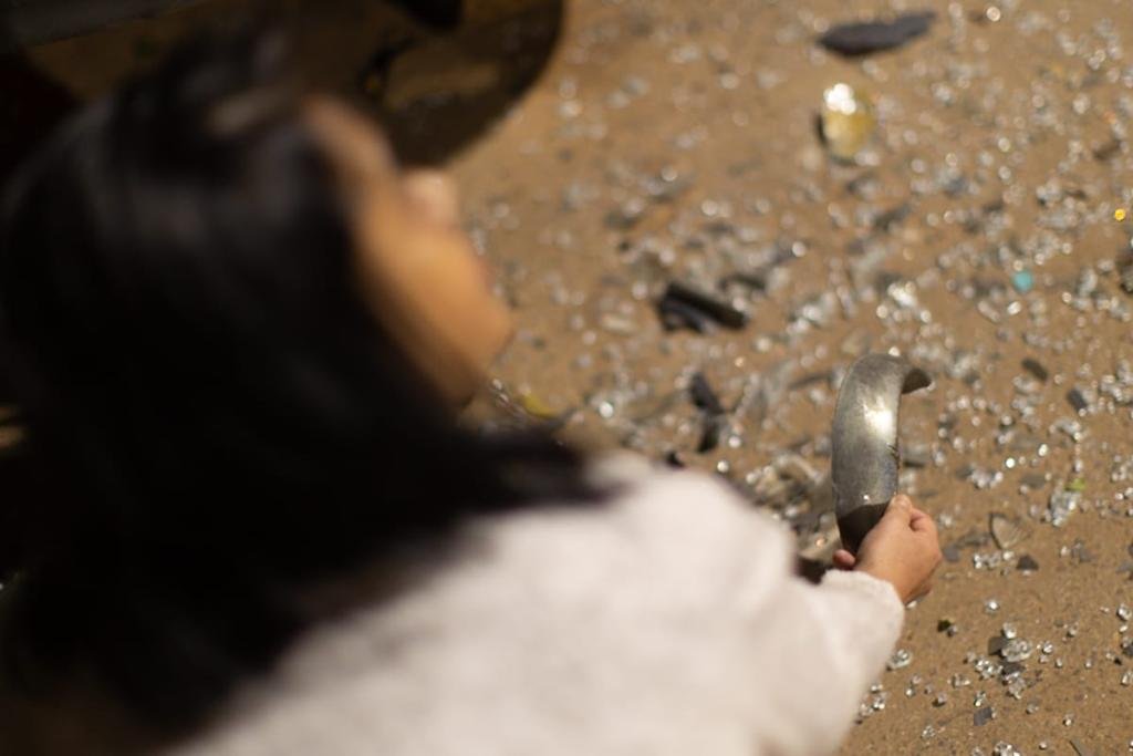 Mulher agachada mostra cacos de vidro de janelas de caminhão depredado por moradores revoltados com idoso que atirou em adolescente, no DF - Metrópoles