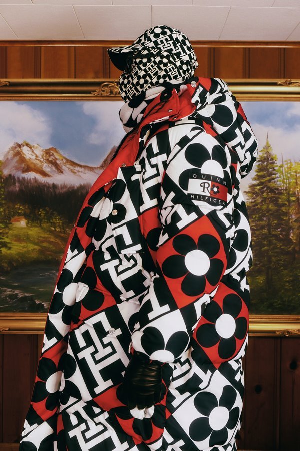 Fotos de campanha da coleção da Tommy Hilfiger com o estilista Richard Quinn. Uma mulher jovem e de pele branca está em uma sala com móveis antigos e usa vestido, meia calça, casaco e chapéu, todos os itens em uma estampa preto e branca com detalhes vermelhos. 