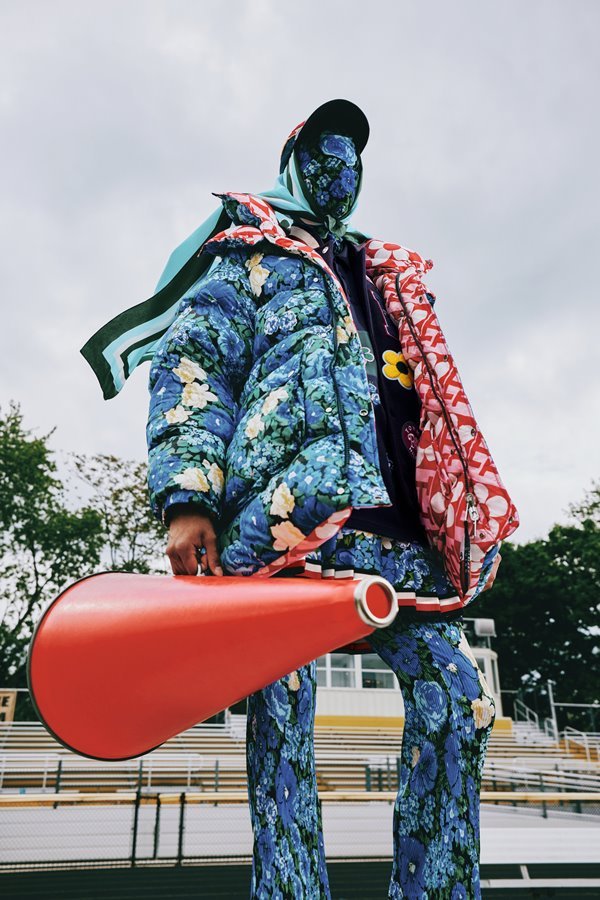 Fotos de campanha da coleção da Tommy Hilfiger com o estilista Richard Quinn. Uma pessoa não identificada aparece com com o rosto coberto por uma máscara com uma estampa de flores azuis. Essa mesma estampa está no casaco e na calça. 