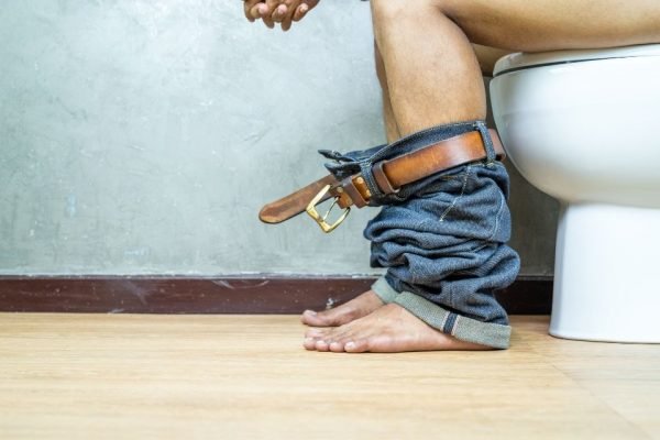Imagem mostra pernas de homem sentado no vaso sanitário - Metrópoles