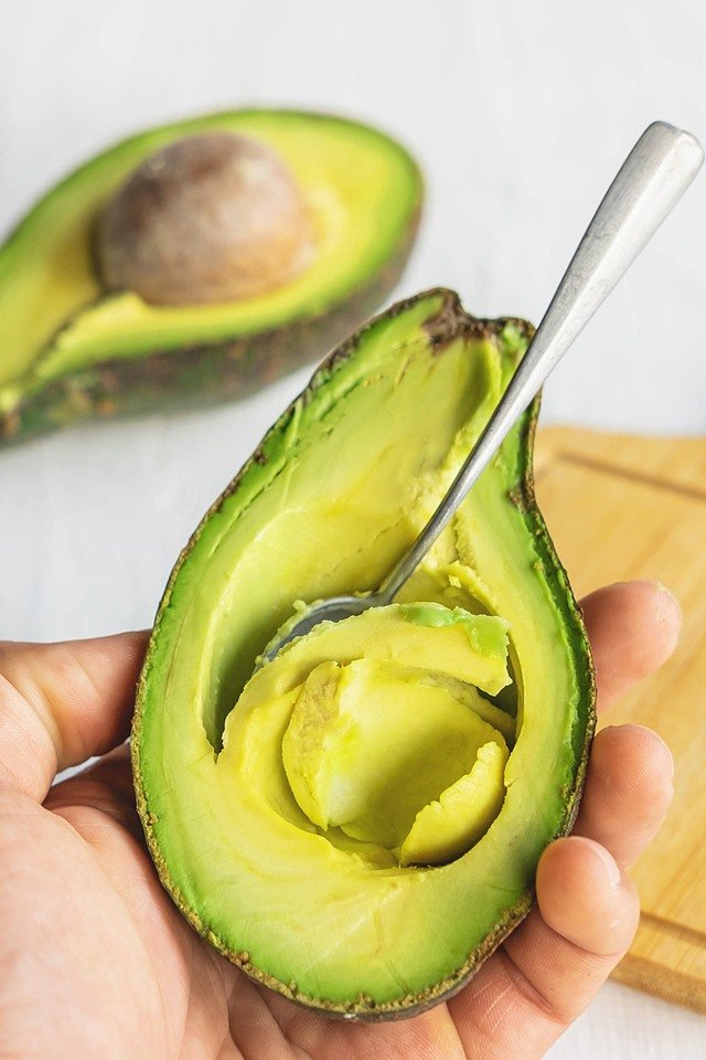 Foto colorida. M&atilde;o segura abacate que tem uma colher dentro