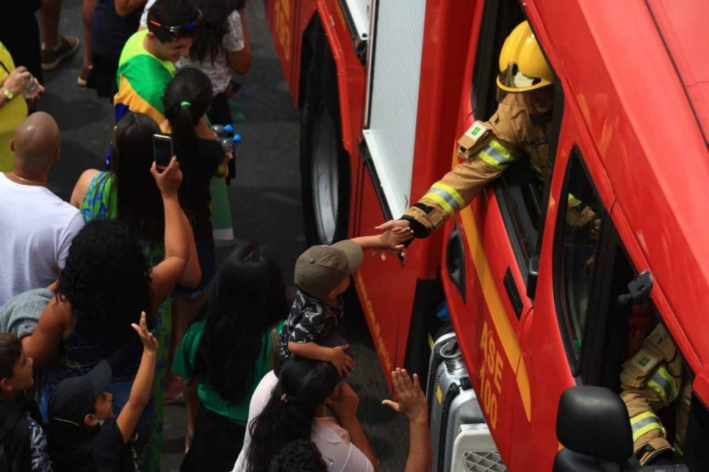 bombeiro dentro do carro oficial estendendo a mão para uma pessoa fora do carro