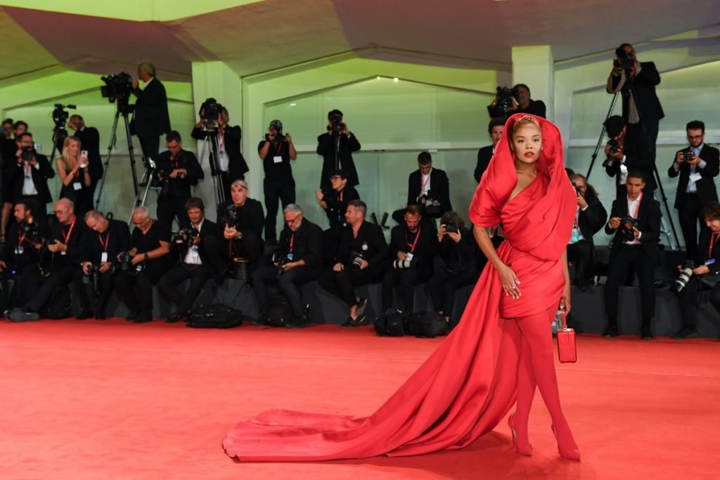 Na imagem com cor, Tessa Thompson usa look vermelho no Festival de Veneza