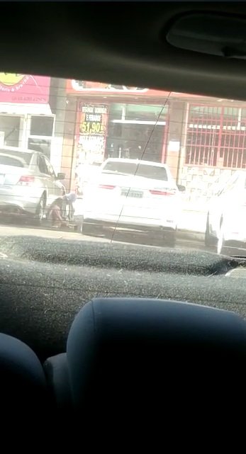 Homem é filmado agachado entre carros estacionados em comércio