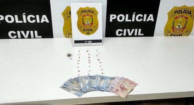 Diversas notas de dinheiro e pedras de crack em cima de mesa branca. Emblema da PCDF