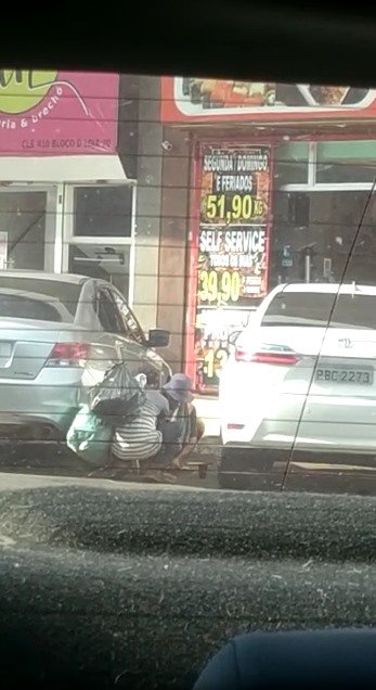 Dupla de homens agachados entre carros estacionados em comércio local