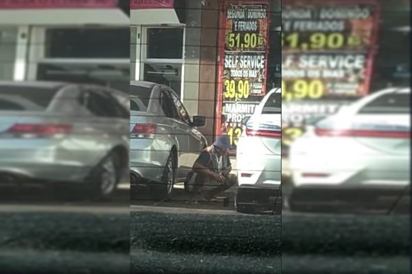 Homem é filmado agachado entre carros estacionados em comércio