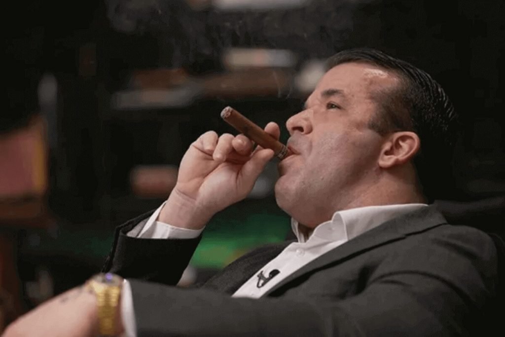 Imagem colorida mostra o empresário Thiago Brennand vestindo um blaser cinza e uma camisa branca. Ele está de perfil fumando um charuto - Metrópoles