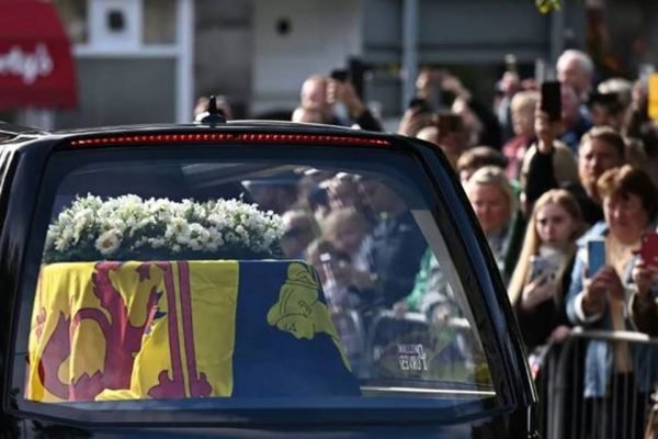 foto colorida de caixão dentro de um carro com coroa de flores em cima