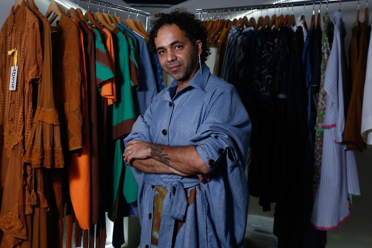Homem preto posando em frente a arara de roupas
