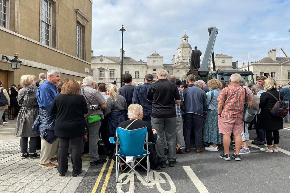 Idoso sentado em cadeira e pedestres em pé, em rua próxima ao Palácio de Westminster, onde aguardam pela chegada do caixão da rainha Elizabeth II