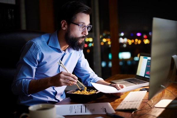 Homem come à noite em frente ao computador