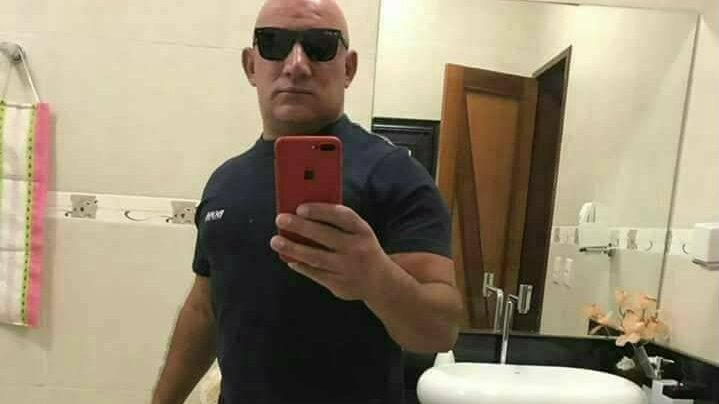 foto colorida de homem na frente de espelho de óculos escuro e camisa preta