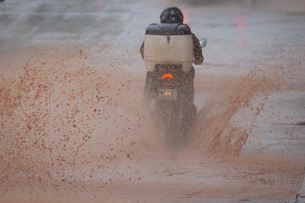 motoboy passa por poça de agua após chuva em brasília