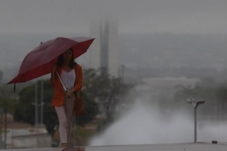 mulher com guarda chuva caminha na torre de tv com vista para o Congresso nacional